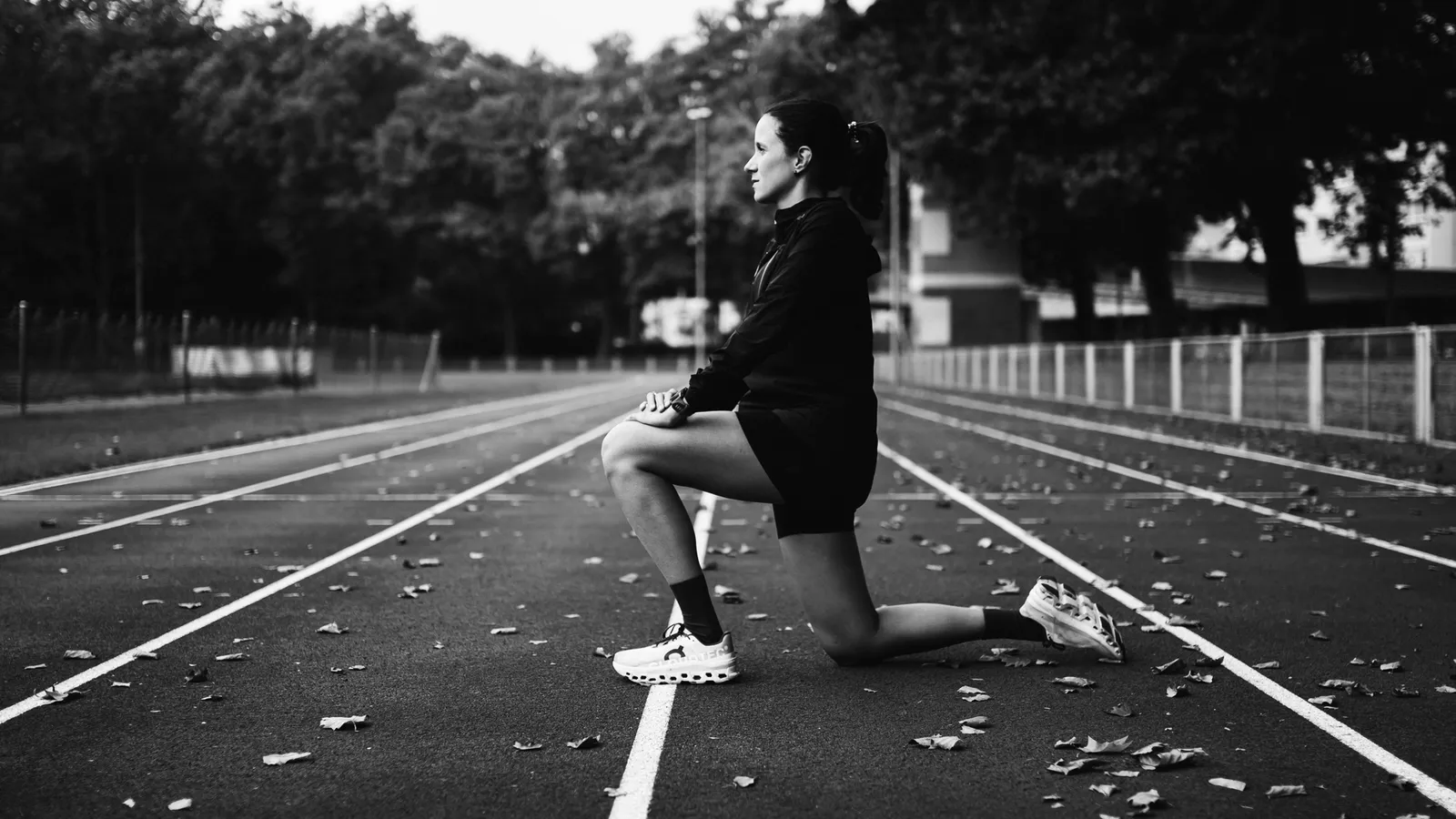 Bruna, augo co-founder and running coach, kneeling in a stretch on an athletics track